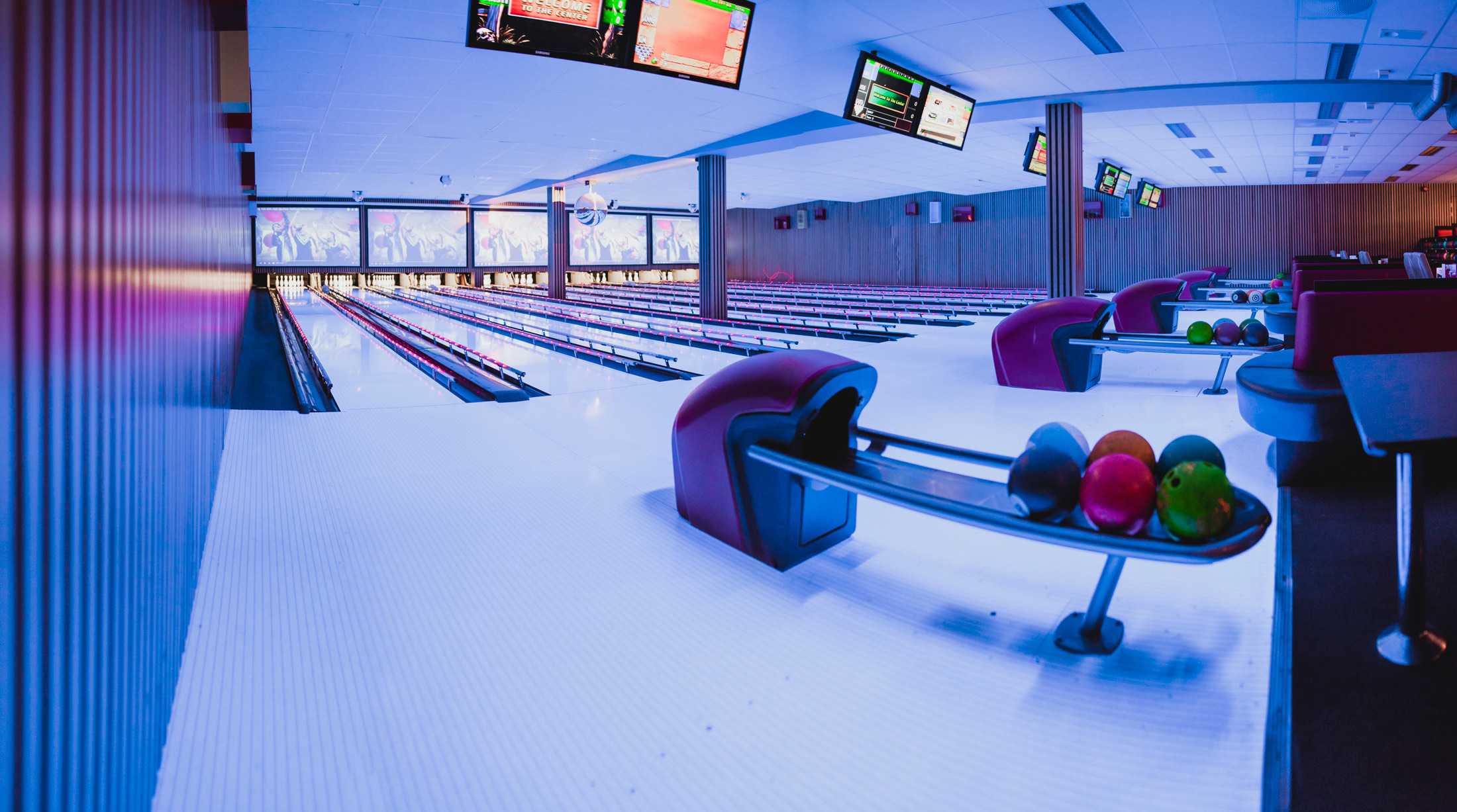Bowling-banene hos Stadion Bowling i Bryne — hvite baner med blå og lilla pubpremium-lys, røde lærsofaer langs sidene og en kuleholder med fire bowlingkuler i forgrunnen