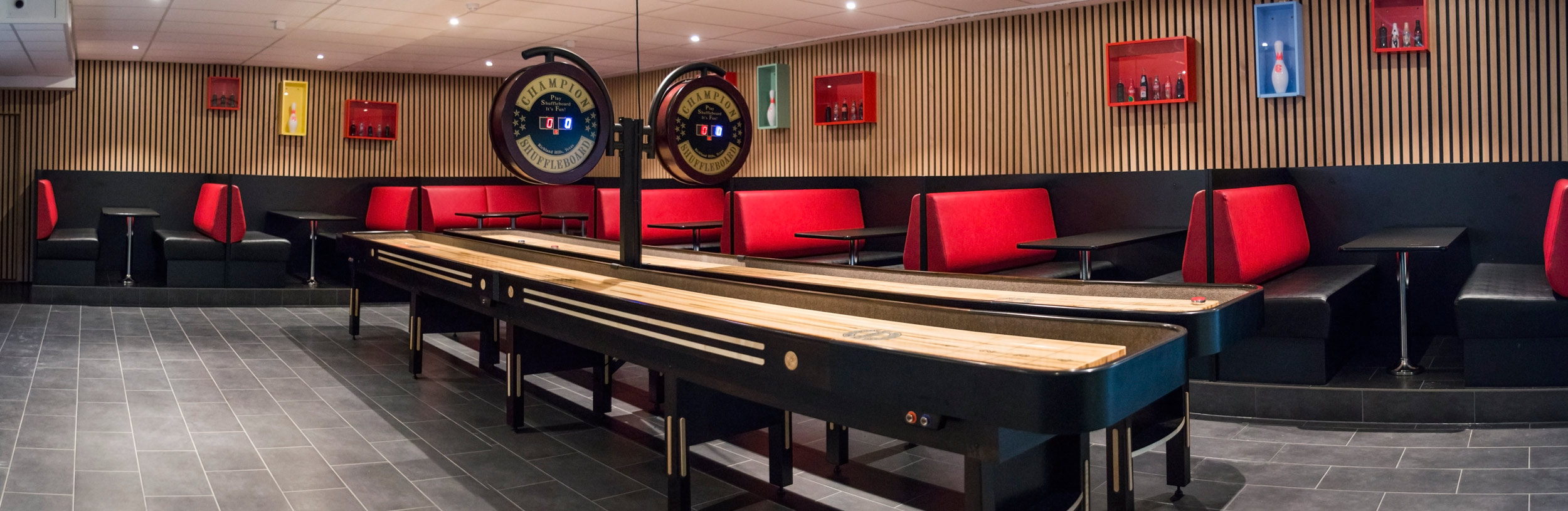 Shuffleboard-arealet hos Stadion Bowling — to lange shufflebord med treverk, røde lærsofaer langs veggene og 'Champion Shuffleboard'-skilt over bordene